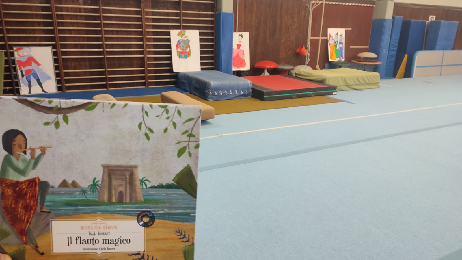 Il libro "Il flauto magico" in primo piano e sullo sfondo un ambiente della palestra.
