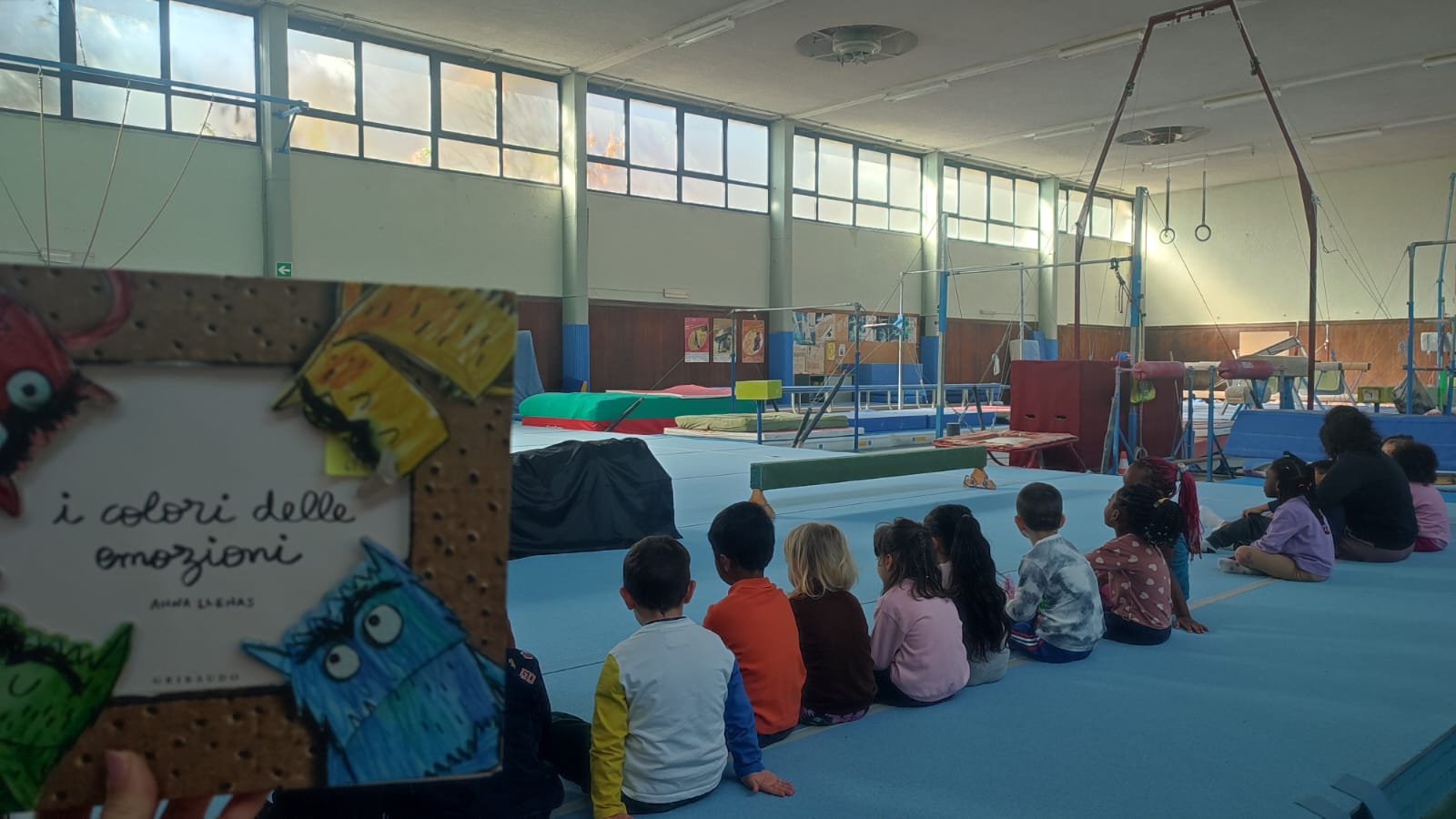 Libro "Il colore delle emozioni" in primo piano e sullo sfondo un gruppo di bambini che svolge l'attività didattica.