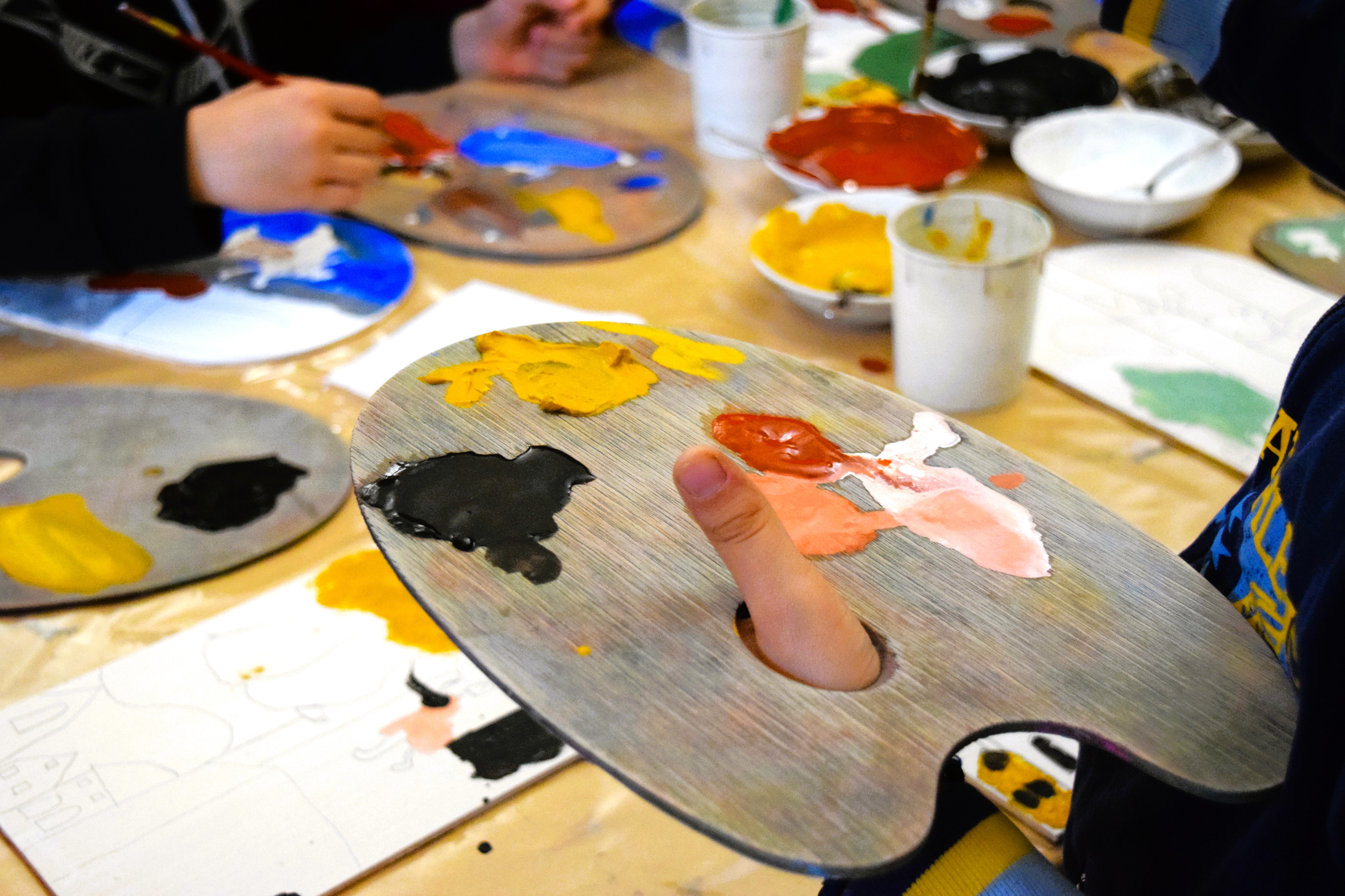 Bambini seduti che dipingono prendendo i colori da tavolozze