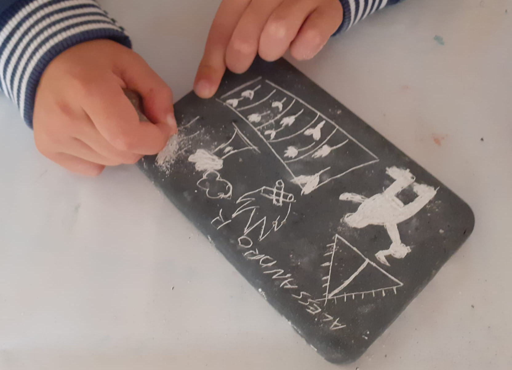 Mani di bambino che scrivono con gesso bianco su piccola lavagna/tavoletta