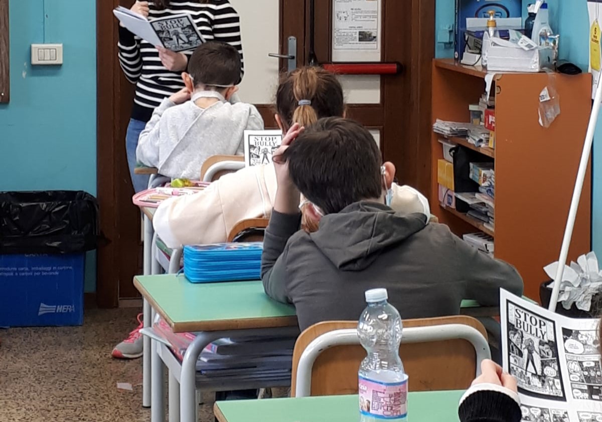 Tre bambini di spalle seduti ai banchi di scuola in fila.