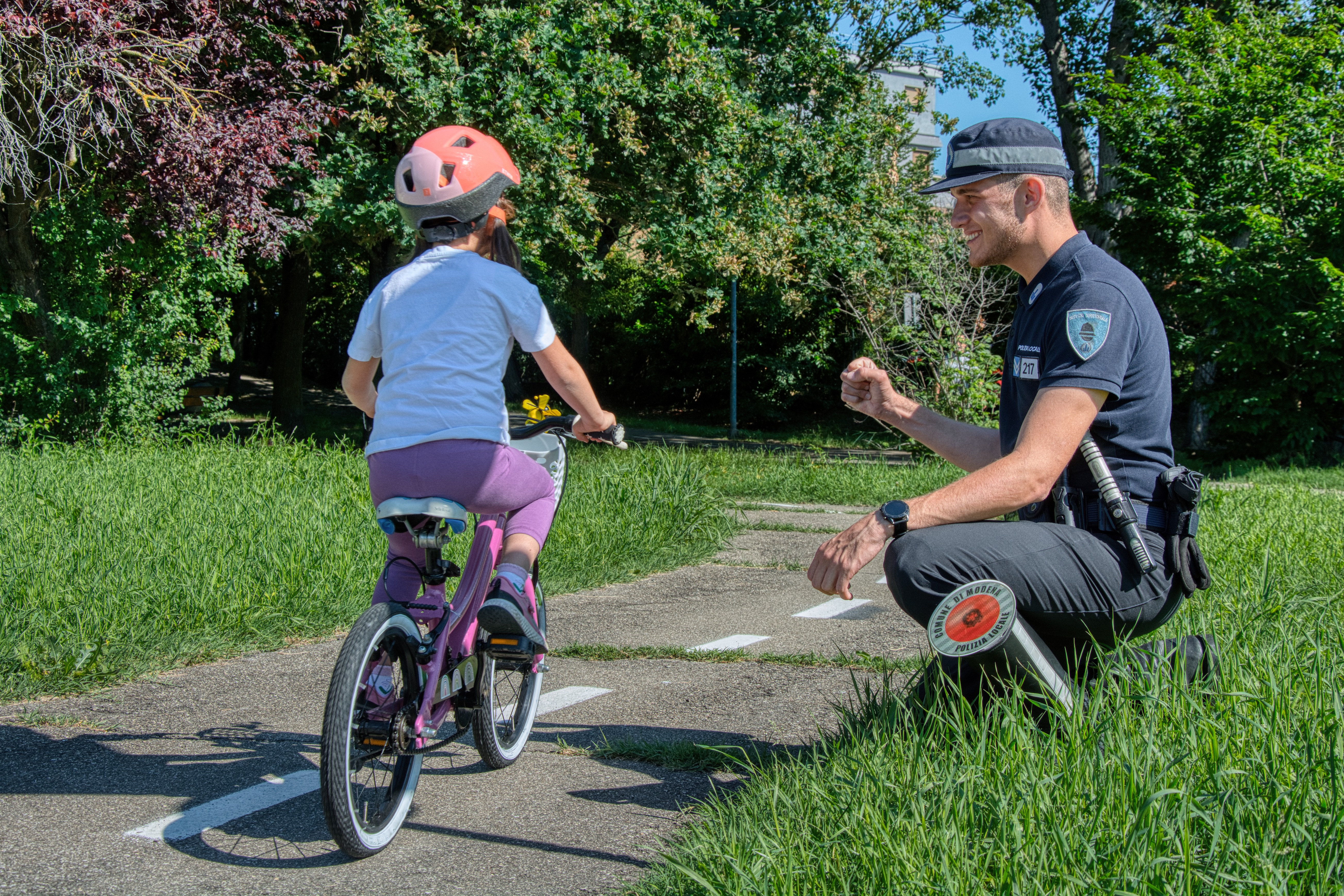 Un bambino sulla bicicletta con un agente vicino che lo osserva sorridendo.