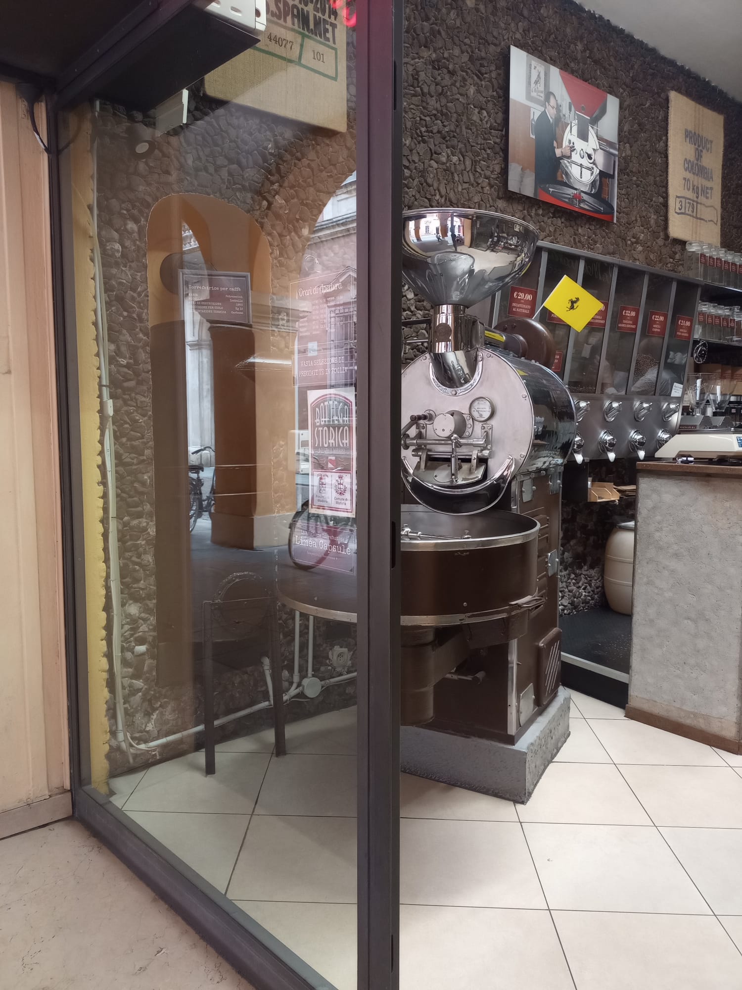 Vetrina di un'antica bottega storica i torrefazione del caffè, con in primo piano una macchina storica per tostare il caffè.